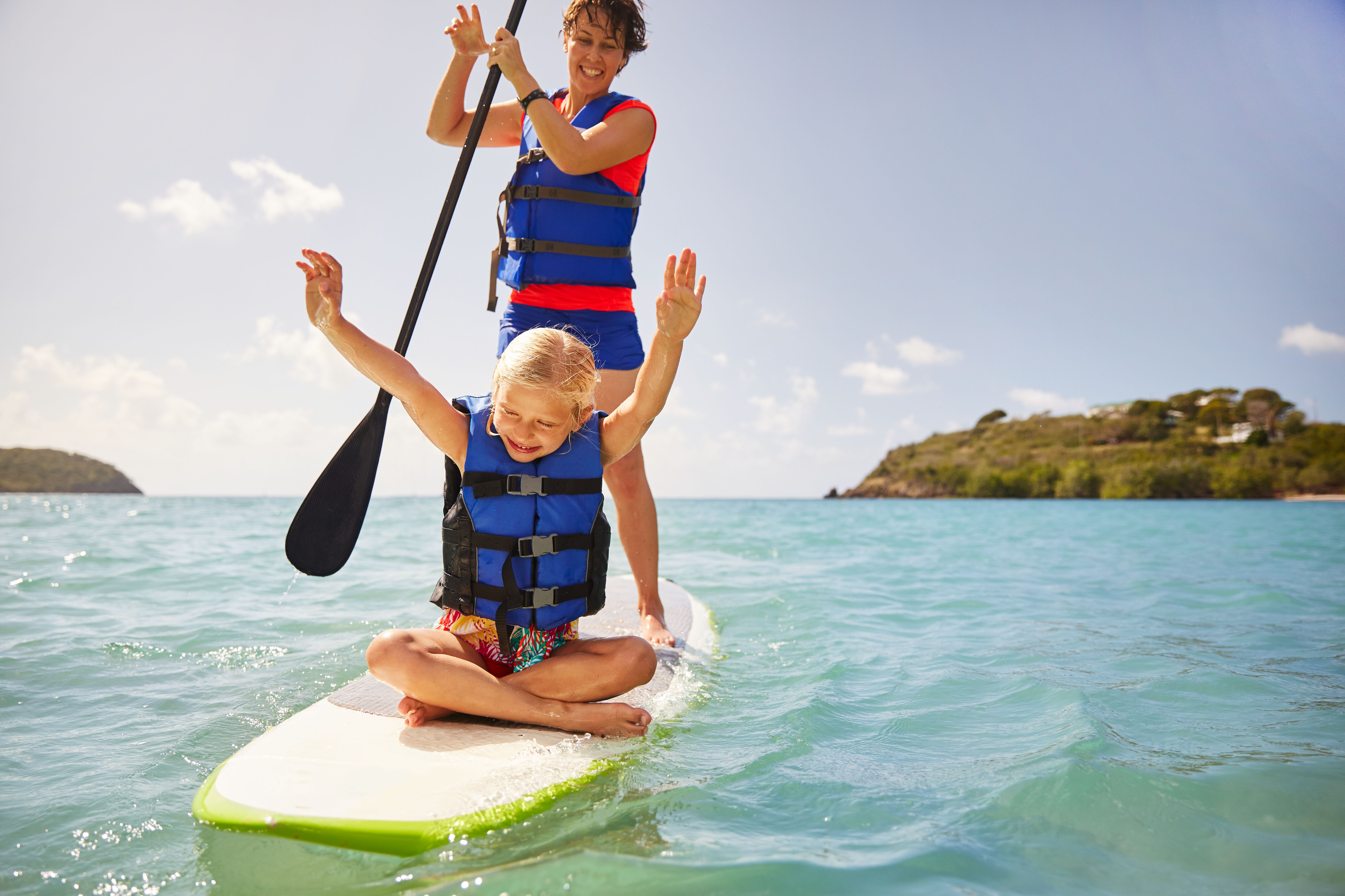 a woman and a little girl with her arms up on a paddleboard